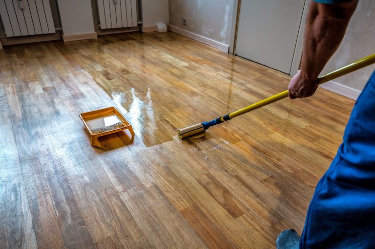 Flooring, Painting & Finishing Parquet floor renovation. Lacquering wood floors. Worker uses a roller to coating floor